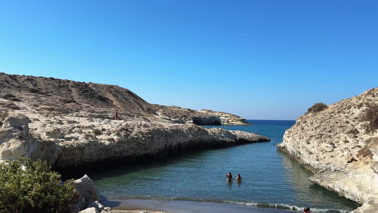 Women swim in the crystal-clear blue waters of Papafragas Beach, enjoying a sunny summer day.