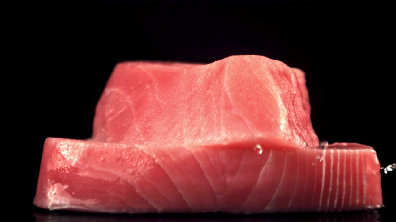 Filete de atún fresco cayendo con salpicaduras de agua sobre fondo negro.