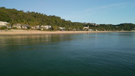 Aerial-Drone-Fly-Low-above-sea-water-coastline,-Australian-Moreton-Island-beach-landscape-in-daylight,-resort-houses,-beachfront