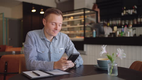 Primer-Plano,-Un-Hombre-Con-Un-Teléfono-Móvil-Se-Dedica-A-Compras-Bancarias-En-Línea-En-Internet-Y-Escribe-Mensajes-En-Redes-Sociales-Mientras-Está-Sentado-Con-Una-Computadora-Portátil