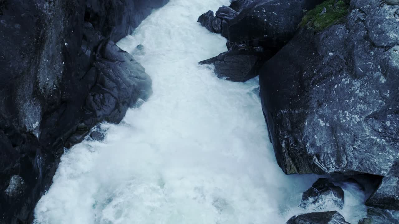 Wild mountain river forces its way through jagged rocks, creating foamy rapids