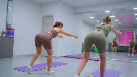 instructor de gimnasia guiando al aprendiz a través del ejercicio de estabilidad mientras equilibran en la sesión de entrenamiento, los espejos del gimnasio reflejan los movimientos, mientras que varios equipos de fitness son visibles en el suelo