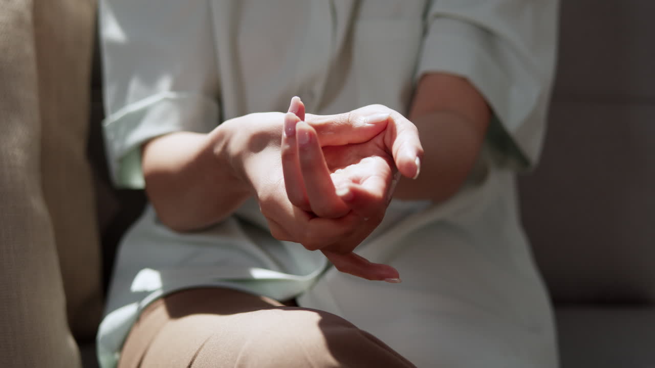 A close-up of an individual massaging her palms using her thumb while sitting on a chair.