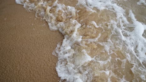 Male-Feet-walking-on-the-sandy-beach-In-The-Foamy-Waves