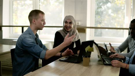 Diverse-People-Using-Laptops-While-Sitting-At-Bright-Work-Place-In-Front-The-Window,-Multi-Ethnic-And-Multi-Cultural-Young-People-Working-As-Team,-Discussing-Start-Up-1