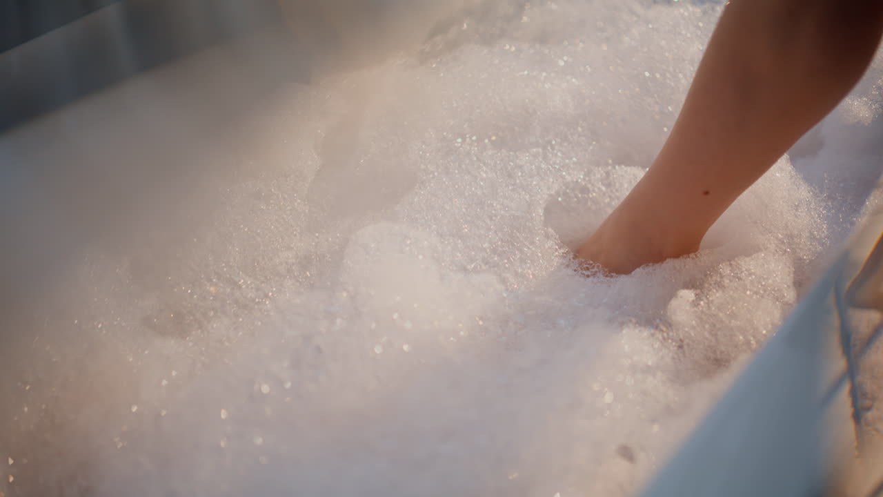 Primo piano di ragazza che immerge la gamba in un bagno schiumoso. Signora in bagno che tocca la schiuma e le bolle.