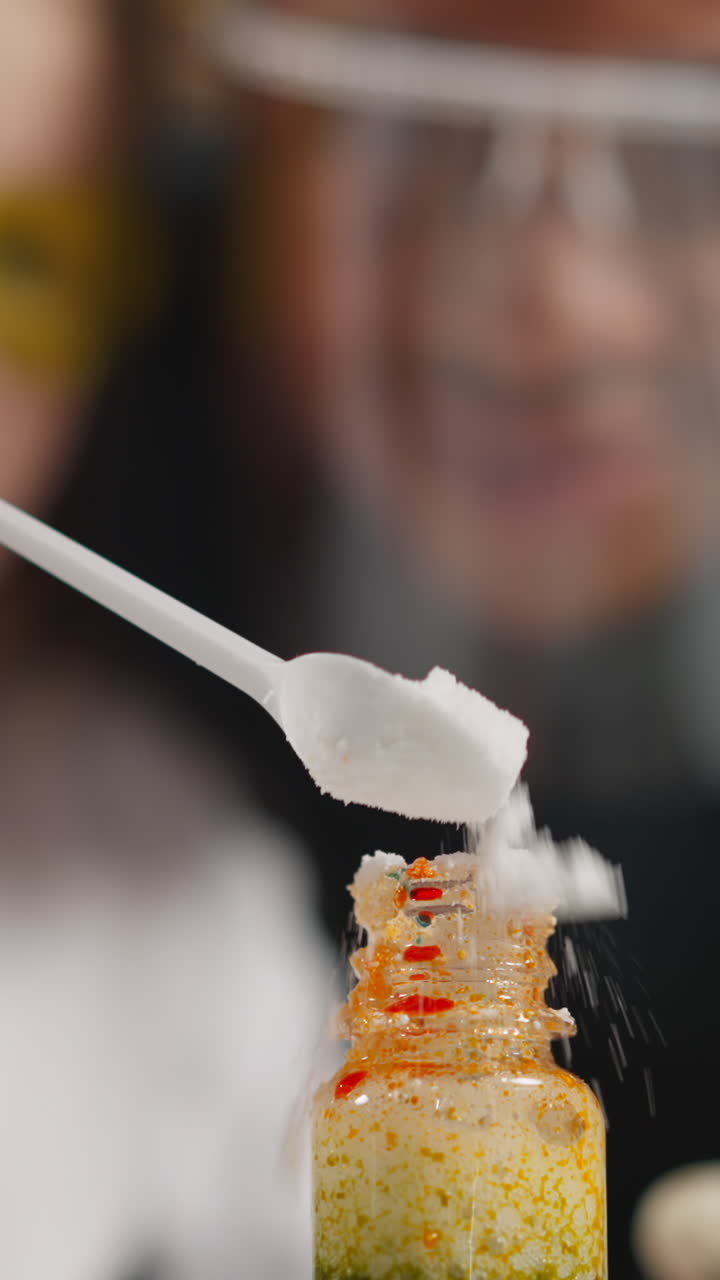 Preschooler girl student pours dry powder yeast into glass bottle providing experiment with African-American teacher in classroom closeup slow motion