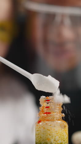 preschooler girl student pours dry powder yeast into glass bottle providing experiment with african-american teacher in classroom closeup slow motion