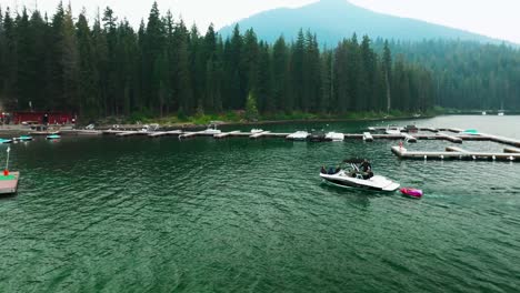 Drone-pan-follows-speed-boat-towing-tube-into-dock-and-marina-in-pine-tree-forest