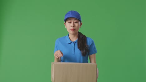 unsatisfied asian female courier in blue uniform shouting to camera while delivering a carton on green screen background in the studio