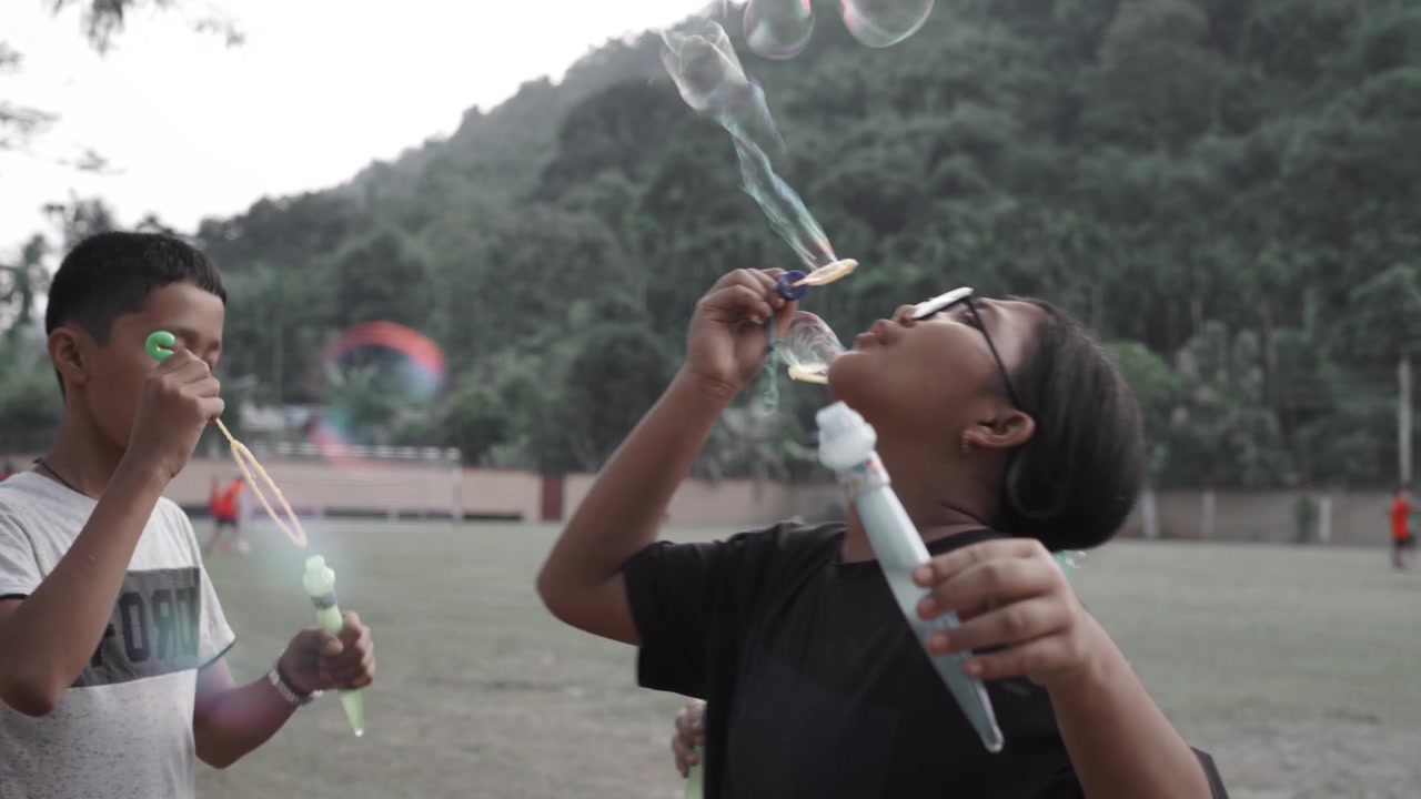 Tiga anak meniup gelembung sabun sambil tersenyum dan merasakan kebahagiaan di taman bermain