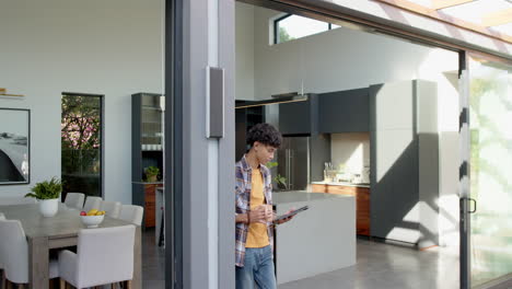 holding tablet and drinking coffee, teenage boy standing in modern kitchen