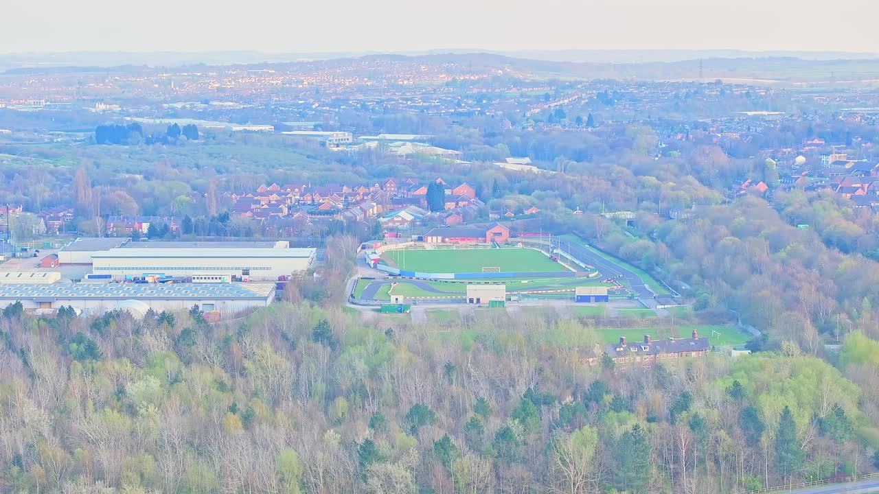 Aerial showing Wombwell karting track and nearby large industrial facility, featuring flat-roofed warehouse with loading bays and vehicle access. surrounded by forested areas and residential zones