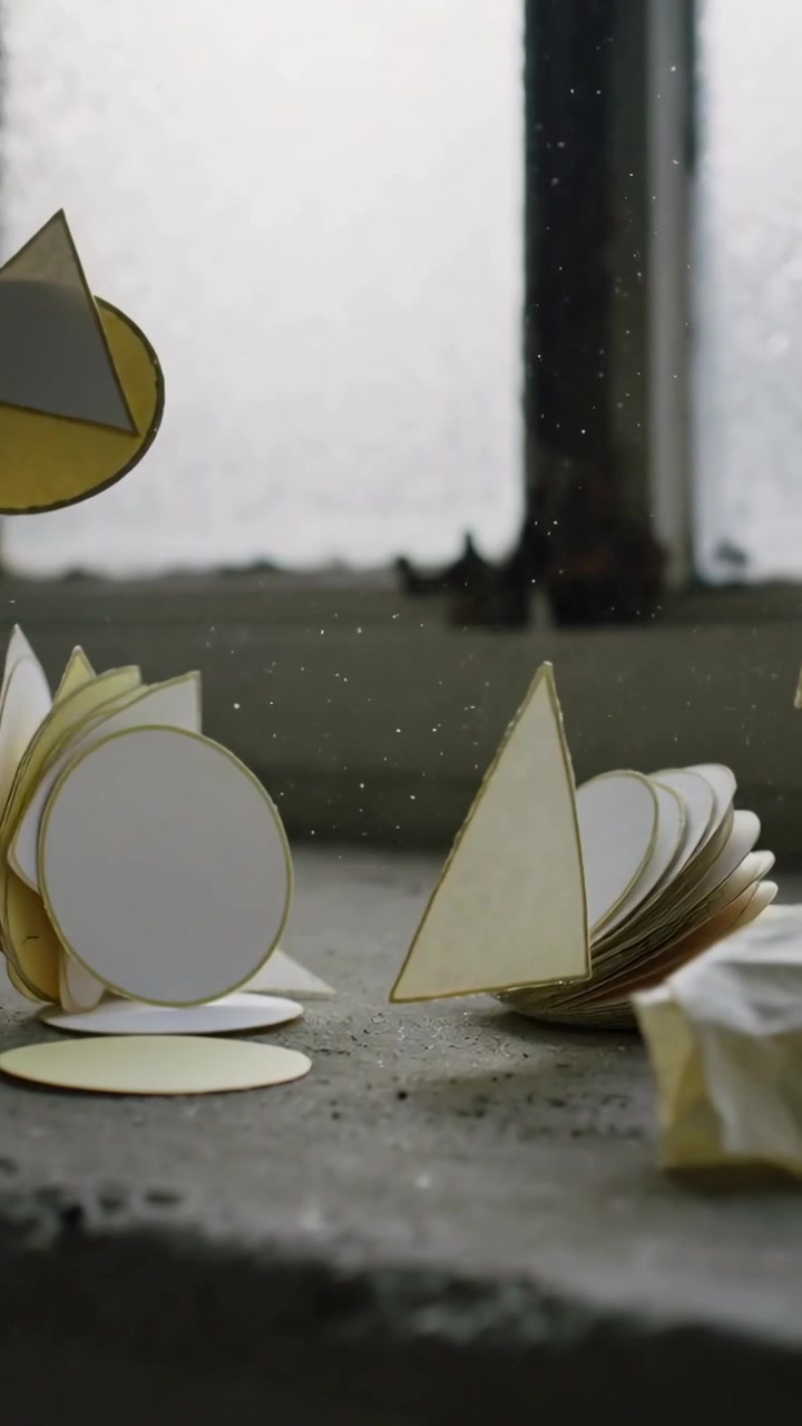Vertical video: Shifting stacks of paper discs and folded triangles tilting on sill, draft passing