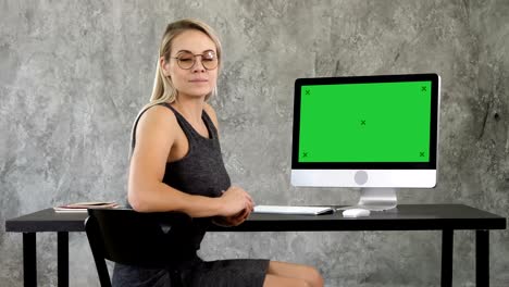 pretty businesswoman looking at camera near computer screen. green screen mock-up display