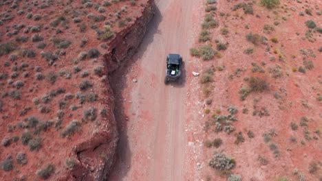 overhead drone shot of off road vehicle driving down a dirt road in the desert