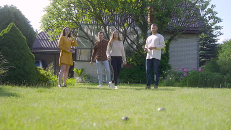 vista lejana de cuatro amigos caucásicos jugando petanca en el parque en un día soleado