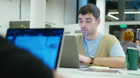 young man using laptop and speaking with colleague in the office