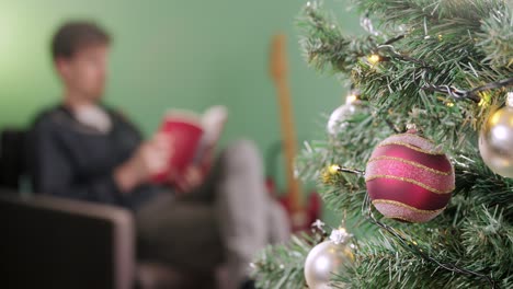 Man-is-relaxing-with-a-book-on-christmas-morning-with-a-christmas-tree-in-the-foreground