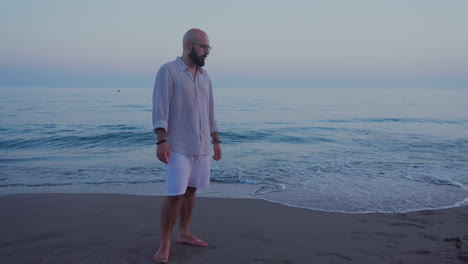 hombre de pie en la playa de arena después del atardecer