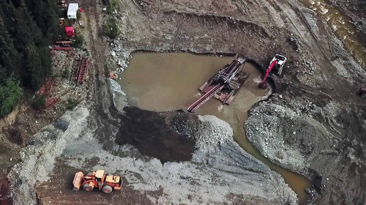 A Bird's Eye View of Excavator Feeding Pay Dirt into Floating Sluice Box Trommel in the Rugged Landscape of the Yukon Territory, Canada