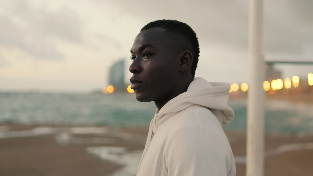 Young Black Man Standing Thoughtfully on a Beach at Dusk