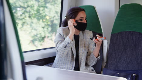 businesswoman on train putting on makeup whilst wearing ppe face mask during health pandemic