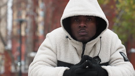 focused military man in winter jacket leans over iron bar, gazing intently with a determined expression, blurred winter background with trees and buildings