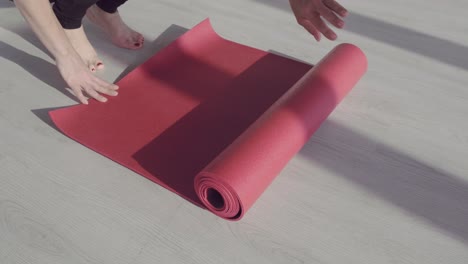 unrolling a red yoga mat on a light wooden floor