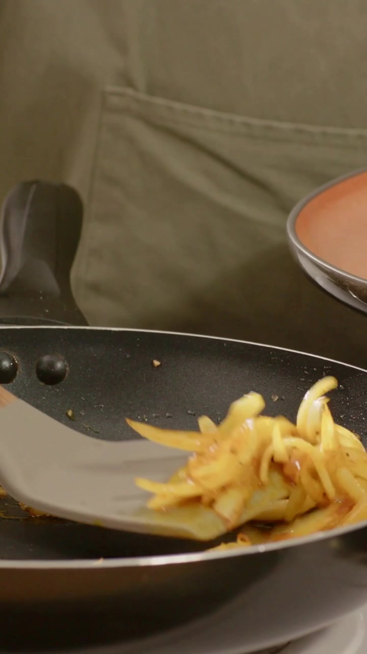 Vertical video: Onions sizzling cook green-apron scraping into orange plate with spatula on stove