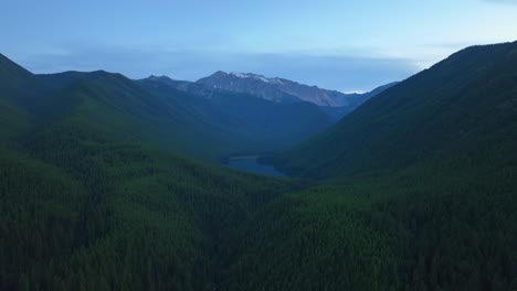 Vista-Aérea-Del-Lago-Stanton-Rodeado-De-Montañas-Boscosas-Y-Nevadas-En-Una-Mañana-Fría-En-El-área-Silvestre-Del-Gran-Oso,-Bosque-Nacional-Flathead,-Montana,-Estados-Unidos