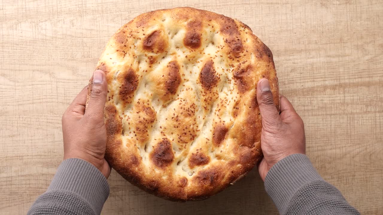 Mani che posano focaccia appena sfornata su un tavolo di legno