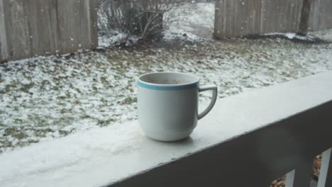 close up on coffee mug on balcony view, snow falling on background, gimbal shot, camera pulling down, day