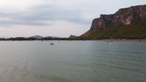 Revealing-Drone-shot-of-Asian-colorful-fishing-boats-at-Khao-Ta-Mong-Lai-Bay-with-rocky-Mountains-on-the-background