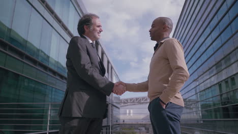 multiethnic businessmen shaking hands on meeting near office building