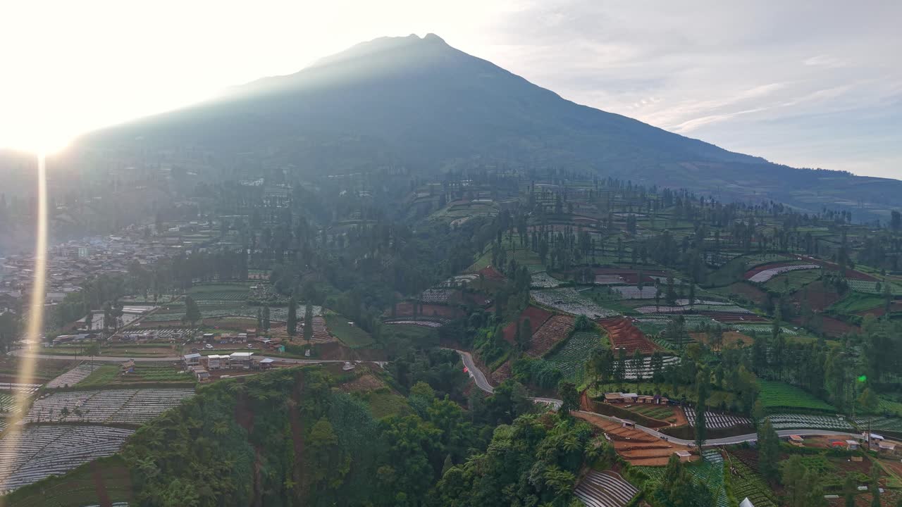 Vista aérea de paisaje montañoso con carretera sinuosa en la ladera, rodeado de exuberantes plantaciones. Campo pintoresco, campos agrícolas y belleza natural bajo una suave luz solar.
