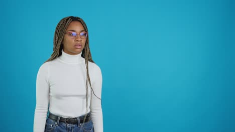 young black woman with braids and glasses showing surprise or concern on blue background