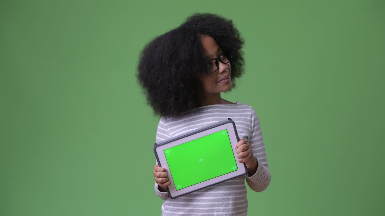 joven chica africana con cabello afro pensando mientras muestra la tableta digital a la cámara