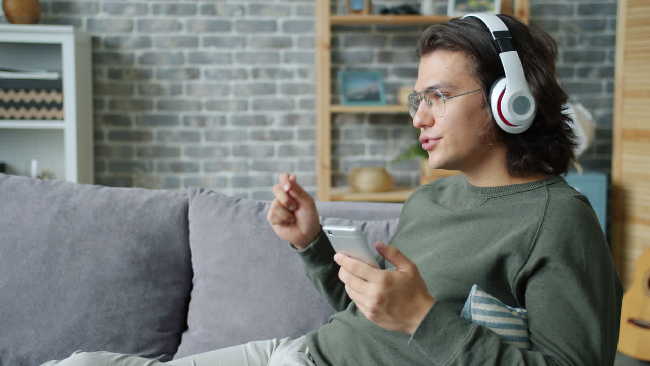 Young Man Relaxing on Couch, Listening to Music and Using Smartphone