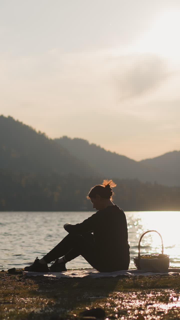 una mujer descansa en un picnic junto al lago al atardecer. una mujer molesta con una canasta de comida hace frente a las emociones negativas de estar sola en vacaciones. sensación de soledad