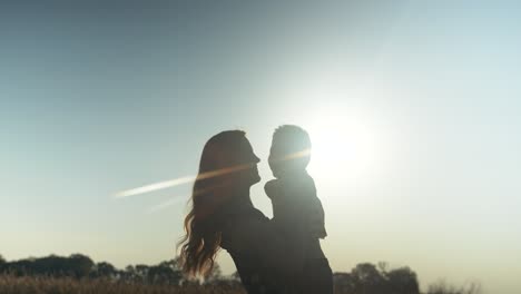 happy, smiling mother and son silhouette, together outside in summer sunset having positive, loving family, parenting or mothers day moment in cinematic slow motion depicting joys of motherhood