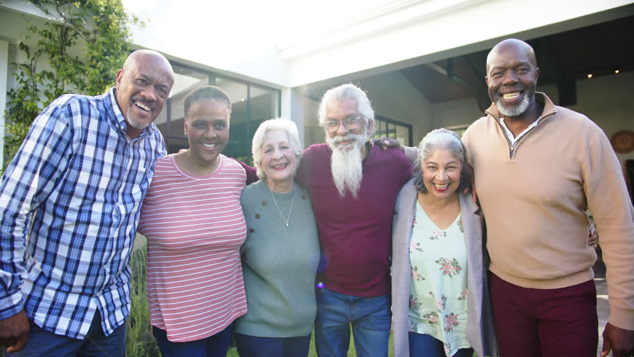Retrato de amigos idosos felizes e diversos (mulheres e homens) abraçando-se em um jardim ensolarado, em câmera lenta
