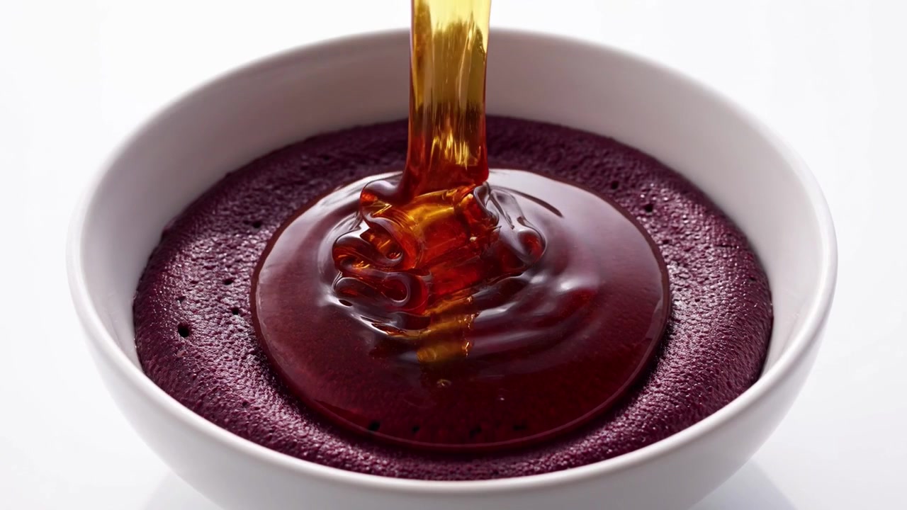 Gyllen honning helles over en glatt lilla acai-bolle