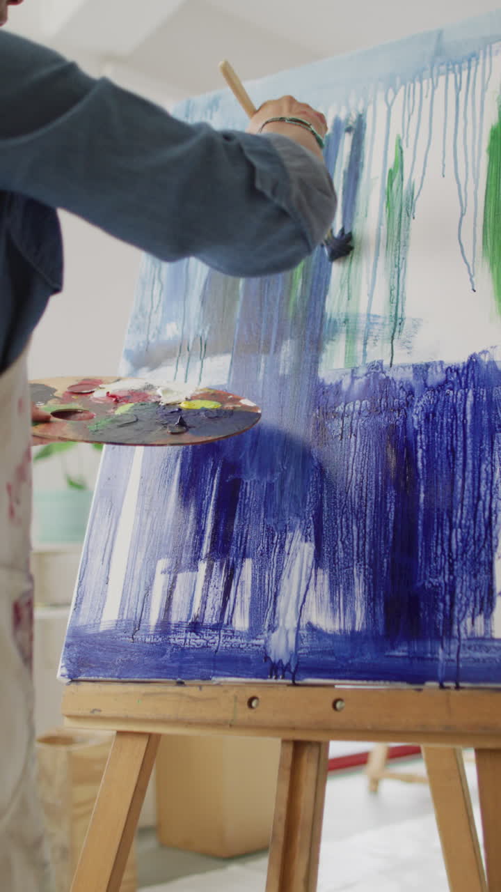 Vertical video of biracial female artist painting in studio