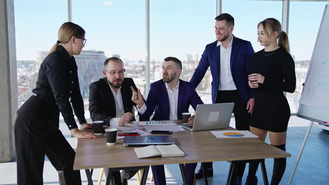 Coworkers having a conversation sitting or standing at the table. Friendly business environment in the office. Colleagues chatting and smiling at work.