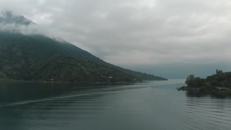 boats sailing on serene lake of atitlan with santiago volcano during misty sunrise in guatemala