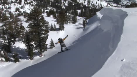 following shot of a snowboarder jump off a slope and landing in deep powder