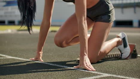 slender young girl athlete is in position to start running in the pads on the track in slow motion