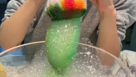 child making a colorful bubble snake using an old sock wrapped over a plastic water. solution is made out of dish soap and water.