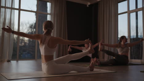 Group-of-young-woman-practicing-yoga-with-the-help-of-an-instructor.-They-are-doing-seated-side-twist-asana.-In-a-bright-room.